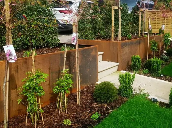 Warm ochre steel tones contrasting with green lawn and stone retaining walls.